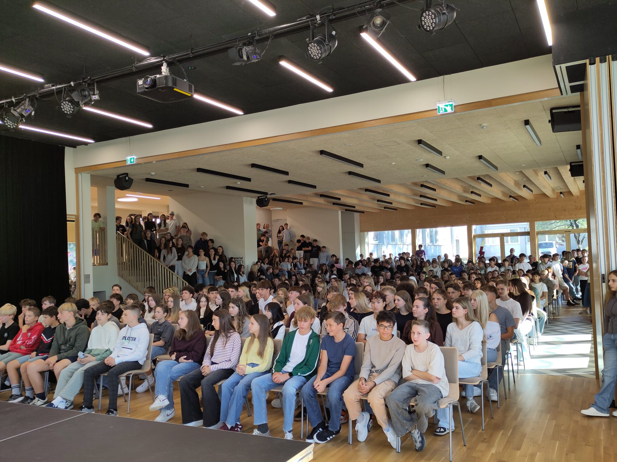 Schülerinnen und Schüler sitzen auf Stühlen in einem großen Veranstaltungssaal.